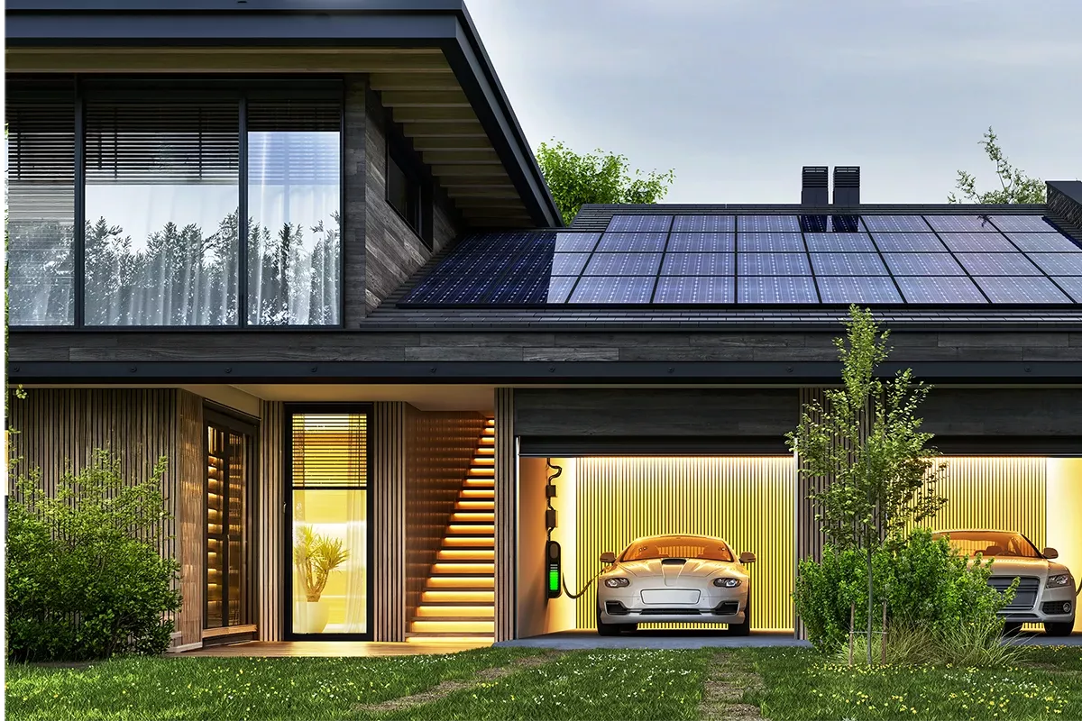 Modern two-story house with rooftop solar panels, illuminated interior, and an electric car charging in an integrated garage at dusk.
